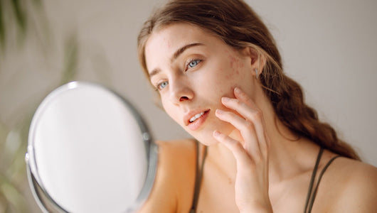 Woman looking in a small round mirror at facial acne, researching the best led face mask for acne treatment