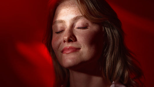 Woman relaxing with eyes closed under red light, illustrating the qure led mask vs omnilux comparison for at-home skincare.