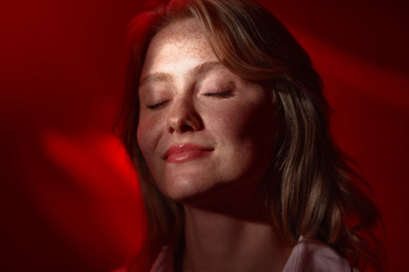 Woman relaxing with eyes closed under red light, illustrating the qure led mask vs omnilux comparison for at-home skincare.
